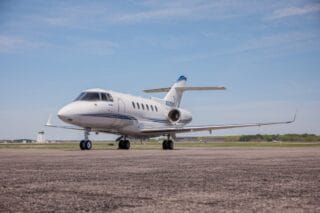 White private jet with blue stripe on tarmac, clear sky.