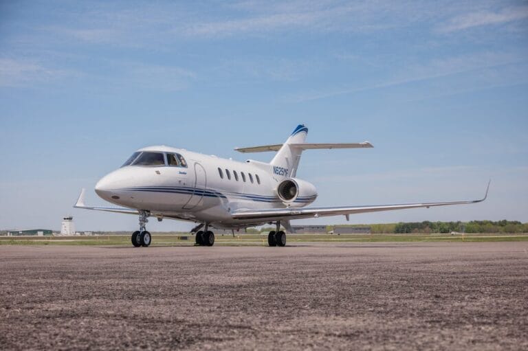 White private jet with blue stripe on tarmac, clear sky.