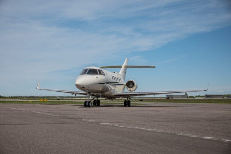White private jet parked on an airport tarmac under a blue sky.