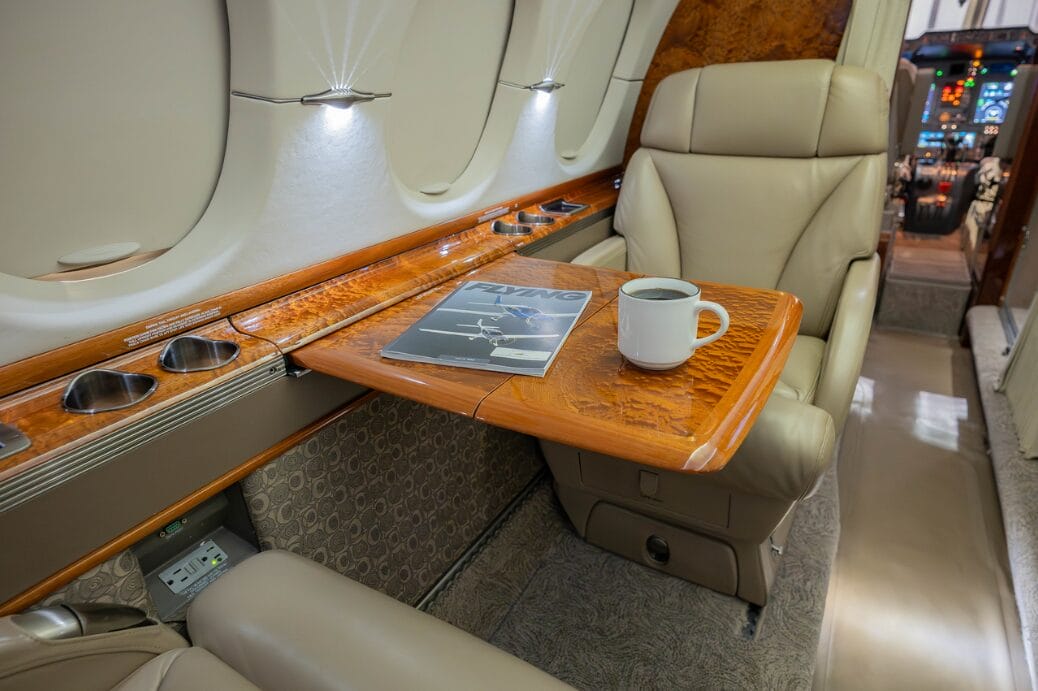 Luxury jet interior with a magazine and coffee on a wooden tray table.