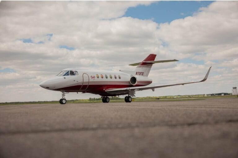 White and red private jet with N79TS on the tail, parked on an asphalt runway under a cloudy sky.