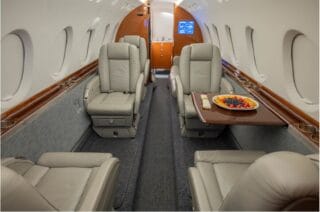 Interior of a private jet with plush leather seats and a tray of fruit.