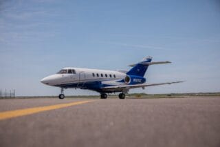 White and blue private jet on tarmac with yellow line.