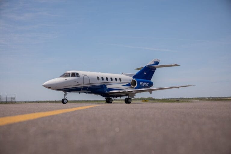 White and blue private jet on tarmac with yellow line.