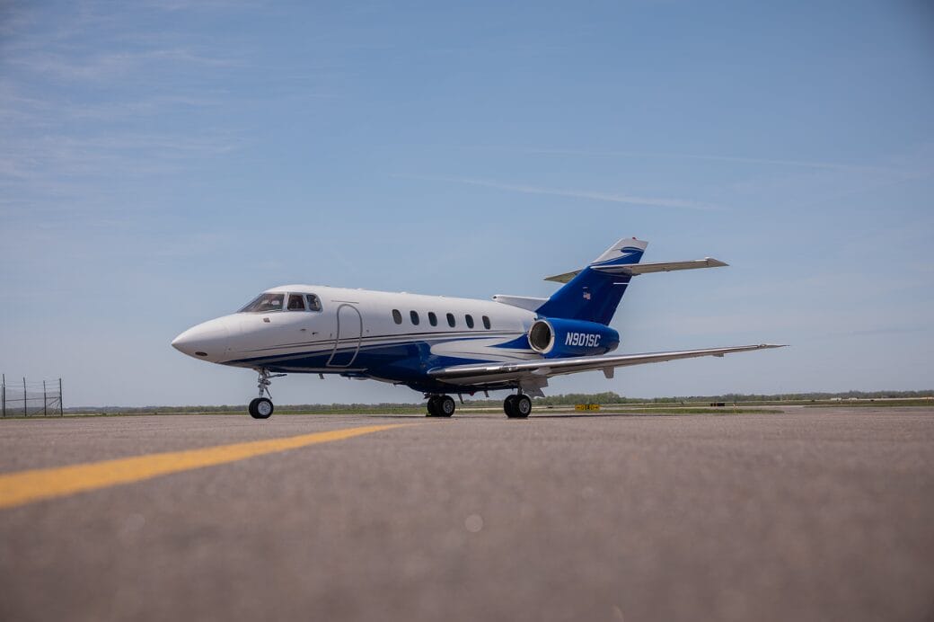 White and blue private jet on tarmac with yellow line.