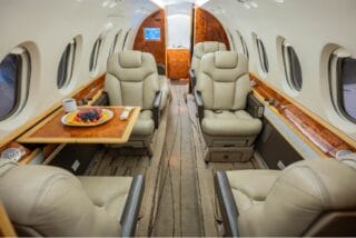 Luxurious private jet interior with plush leather seats and a fruit platter on a tray table.