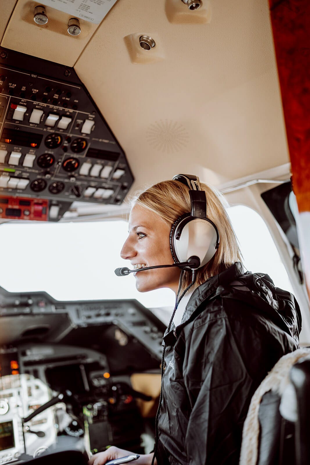Pilot wearing headset in cockpit with control panel.